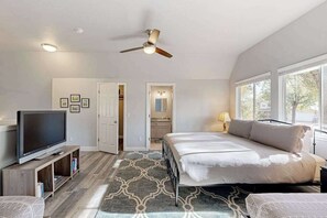 Ein Schlafzimmer mit Bett, Fernseher, Deckenventilator und Blick ins Freie durch große Fenster.