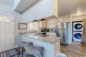 Una cocina moderna con una isla central, taburetes de bar, refrigerador, microondas y lavadora.