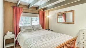 Un dormitorio con cama, mesita de noche, cómoda, espejo y ventana con cortinas.