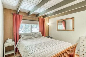 Ein Schlafzimmer mit einem Bett, einem Nachttisch, einer Kommode, einem Spiegel und einem Fenster mit Vorhängen.