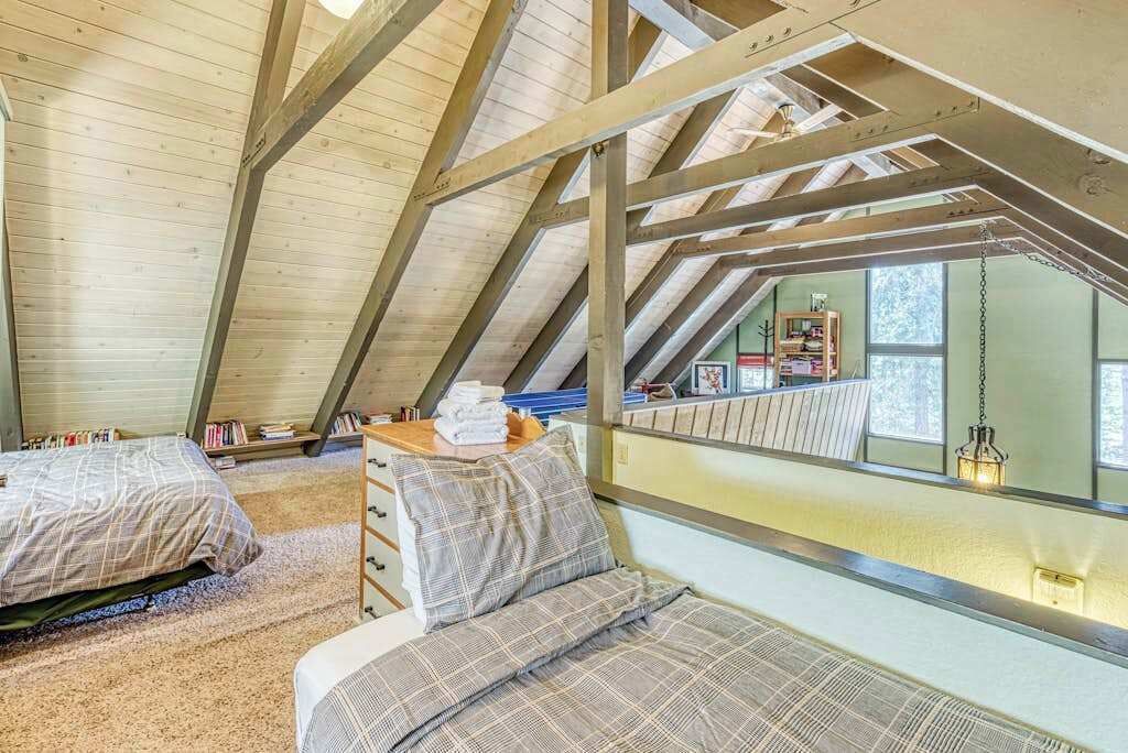 Une chambre aménagée en mezzanine avec un plafond en pente, deux lits, une échelle en bois et une vue sur l’extérieur.