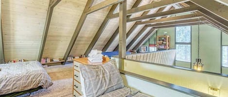 A loft bedroom with a sloped ceiling, two beds, a wooden ladder, and a view of the outdoors.