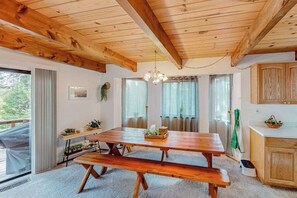 Una mesa de madera con bancos, una cocina con armarios de madera y vistas al exterior a través de grandes ventanas.