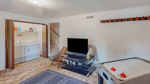 Ein Zimmer mit Waschmaschine, Flachbildfernseher, Spieltisch und Treppe.