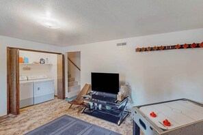 A room with a washing machine, a flat-screen TV, a gaming table, and a staircase. - Forest Retreat - Blue Lake Springs (Arnold)