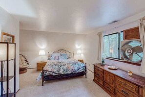 Un dormitorio con cama, lámparas de noche, un ventilador, cómoda y ventana con cortinas.