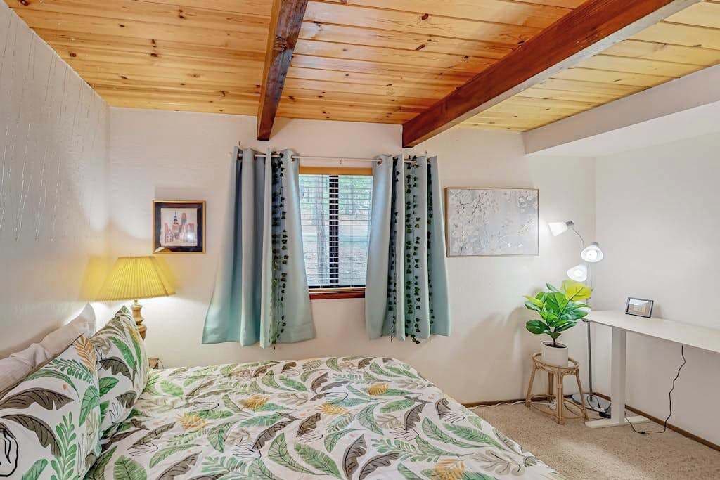 A bedroom with a bed, a desk, a lamp, a window with curtains, and a wall-mounted picture.
