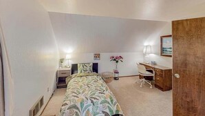Ein Schlafzimmer mit Bett, Nachttisch, Lampe, Schreibtisch, Stuhl und einer Tür.