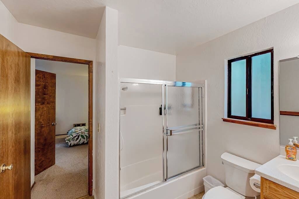 A bathroom with a glass shower enclosure, a toilet, and a sink with a mirror above it.