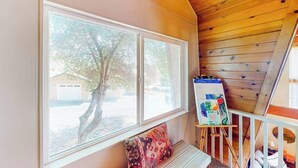 A room with a large window, a bench, and an easel with a painting. - Cozy Cabin - Pine Mountain Lake (Groveland)