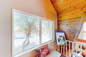 A room with a large window, a bench, and an easel with a painting. - Cozy Cabin - Pine Mountain Lake (Groveland)
