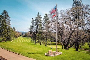 Un campo de golf con una bandera, árboles y cielo despejado.
