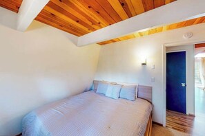 A bedroom with a wooden ceiling, a bed with pillows, a nightstand, and a door leading to another room. - Cozy Cabin - Pine Mountain Lake (Groveland)