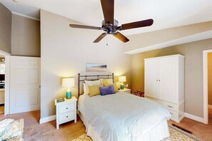 Une chambre à coucher comprenant un lit, des tables de chevet, un ventilateur de plafond, une armoire et un tableau accroché au mur.