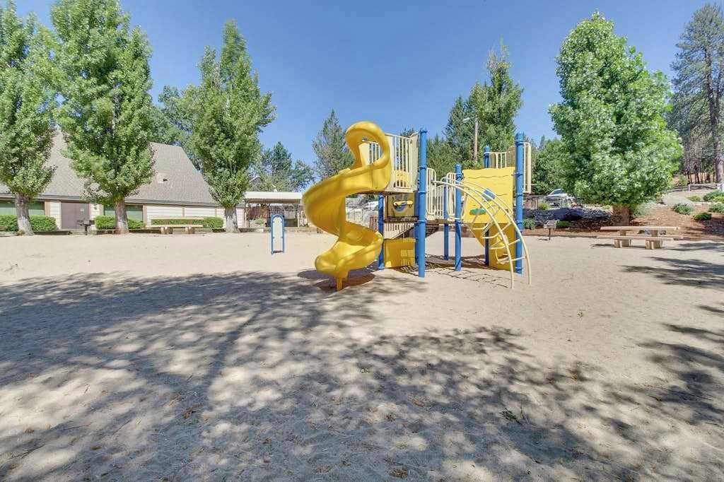 A playground with a yellow slide and climbing structures, surrounded by trees and a building in the background.
