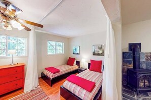 A bedroom with two beds, a red dresser, a wooden ceiling fan, a stone fireplace, and a window with a view of trees. - The Lake Haus - Pine Mountain Lake (Groveland)