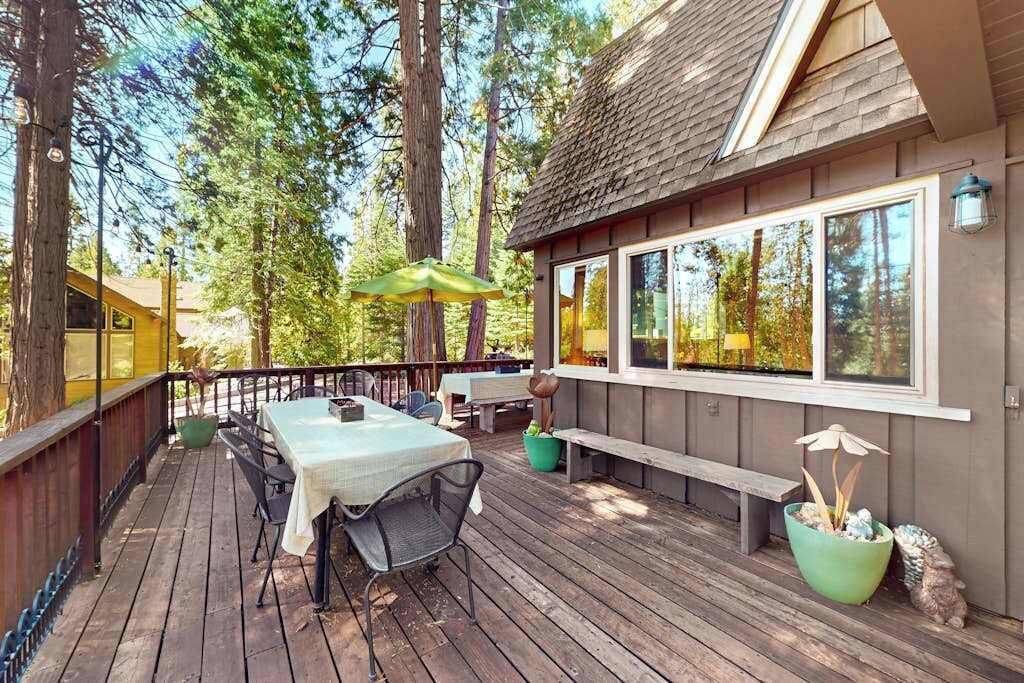 Eine Holzterrasse mit Tisch und Stühlen, umgeben von hohen Bäumen.