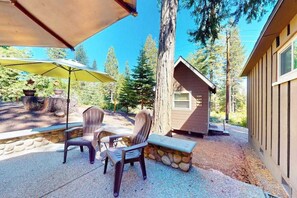 Eine Terrassenausstattung mit zwei Stühlen, einem Tisch, einer Steinsitzbank und einer kleinen, hüttenähnlichen Struktur.