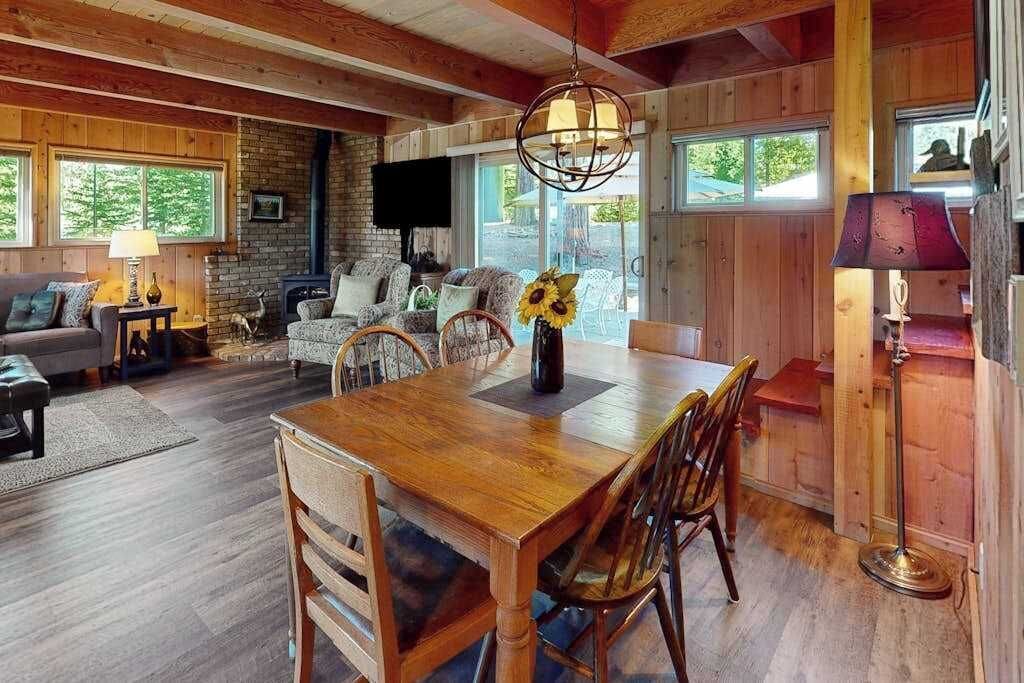 A wooden dining table with chairs, a fireplace, and a television in a cozy room with wooden walls and large windows.