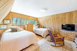 Ein Schlafzimmer mit zwei Betten, einer Holzkommode, einem Fernseher und gerahmten Bildern an der Wand.