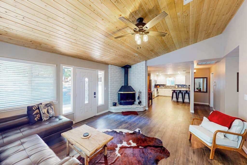 A spacious living area with a fireplace, wooden ceiling, and a modern kitchen in the background.