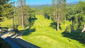 Un campo de golf con vista despejada al fairway, rodeado de árboles y una cordillera distante.