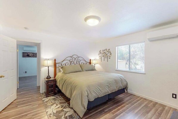 Un dormitorio con cama, lámparas de noche, una ventana y una puerta que da a otra habitación.