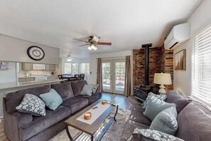 A living room with a sofa, coffee table, and a fireplace. There is a kitchen area with cabinets and a dining table. - Holiday Chalet - Pine Mountain Lake (Groveland)