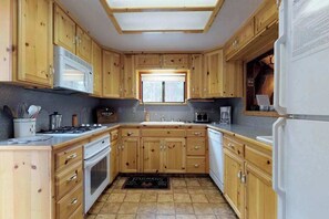 A kitchen with wooden cabinets, a microwave, a stove, and a refrigerator. - Foxtail Delight - West Village (Shaver Lake)