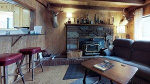 A rustic interior with a stone fireplace, wooden walls, a sofa, and a bar area with stools. - Foxtail Delight - West Village (Shaver Lake)