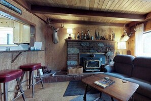 A rustic interior with a stone fireplace, wooden walls, a sofa, and a bar area with stools. - Foxtail Delight - West Village (Shaver Lake)