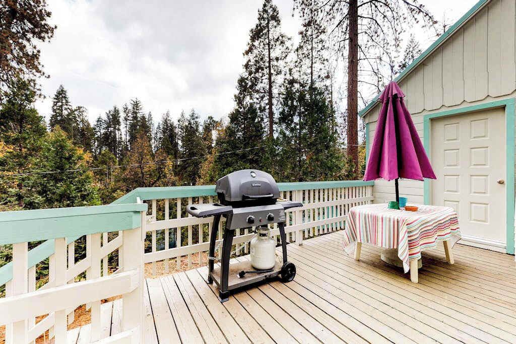 Eine Terrasse mit Grill, einem Tisch mit gestreiftem Tischläufer und einem violetten Sonnenschirm.