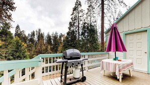 A deck with a barbecue grill, a table with a striped tablecloth, and a purple umbrella. - Foxtail Delight - West Village (Shaver Lake)