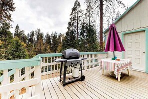 A deck with a barbecue grill, a table with a striped tablecloth, and a purple umbrella. - Foxtail Delight - West Village (Shaver Lake)
