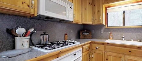 A kitchen with wooden cabinets, a microwave, a gas stove, and a sink.