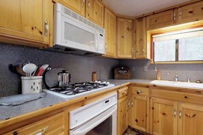 Une cuisine avec des meubles de rangement en bois, un four à micro-ondes, une cuisinière à gaz et un évier.