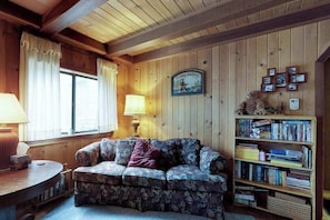 Een gezellige kamer met een bloemenbank, een houten boekenplank en een bord aan de muur.