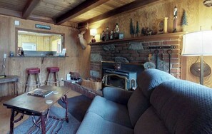 Ett mysigt vardagsrum med en öppen spis, träpanel på väggarna, en soffa och ett bord med en lampa.