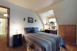 Een slaapkamer met een bed, nachtkastje, lamp en een bureau met stoel.