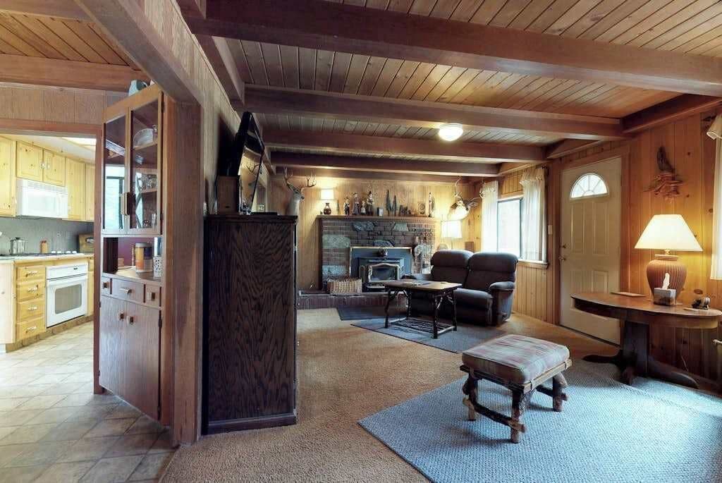 A rustic interior with a kitchen, dining area, and living room, featuring wooden beams, a fireplace, and a stone fireplace surround.