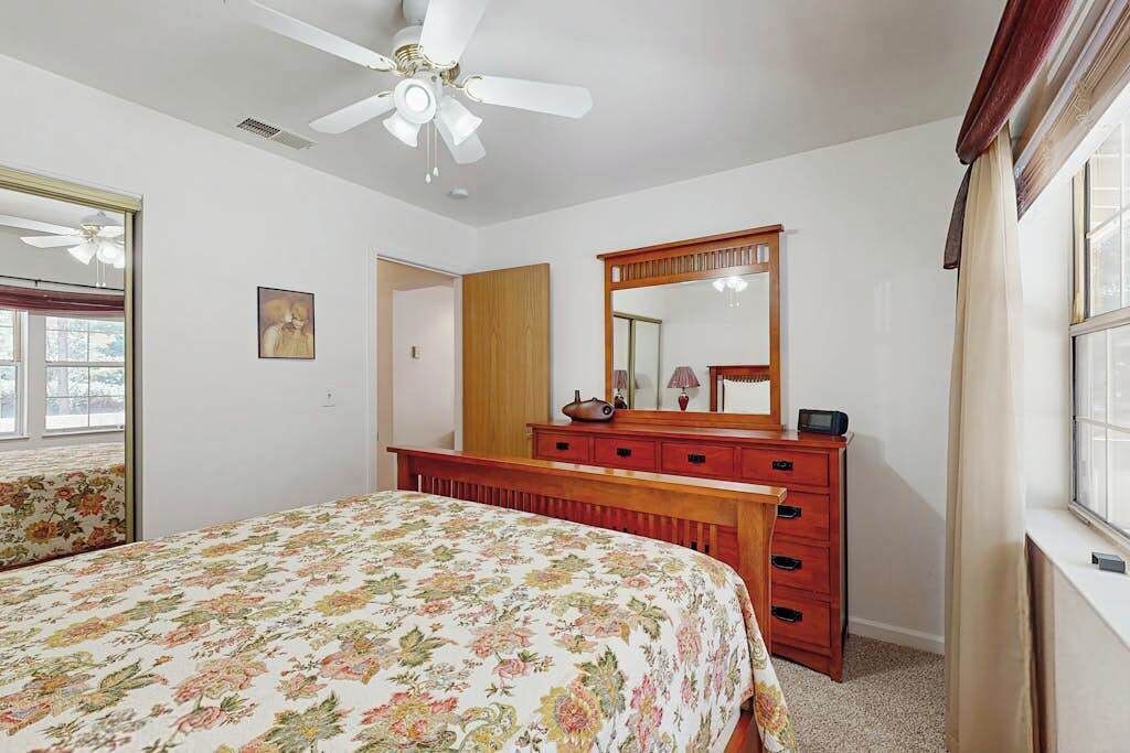A bedroom with a bed, a dresser, a mirror, and a ceiling fan.
