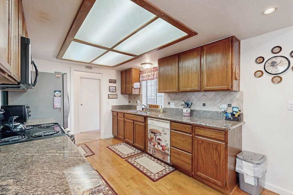 Una cocina con armarios de madera, encimera de granito, lavavajillas y tragaluz.