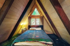 A triangular attic bedroom with a bed, a nightstand, and a window. - Under The Trees - Big Trees Village (Camp Connell)
