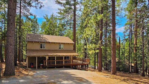 A two-story cabin with a covered porch and a garage, surrounded by tall pine trees. - Bigfoot Cabin - Big Trees Village (Camp Connell)