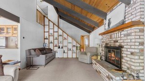 A spacious living area with a fireplace, a staircase, and a bookshelf. - Bigfoot Cabin - Big Trees Village (Camp Connell)