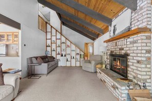 A spacious living area with a fireplace, a staircase, and a bookshelf. - Bigfoot Cabin - Big Trees Village (Camp Connell)