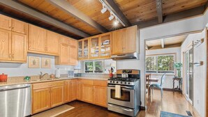 A modern kitchen with wooden cabinets, stainless steel appliances, and a view to the dining area. - Bigfoot Cabin - Big Trees Village (Camp Connell)