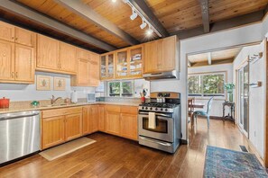 A modern kitchen with wooden cabinets, stainless steel appliances, and a view to the dining area. - Bigfoot Cabin - Big Trees Village (Camp Connell)