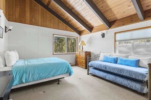 A bedroom with two beds, a dresser, a lamp, and large windows. - Bigfoot Cabin - Big Trees Village (Camp Connell)