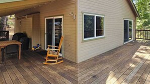 A wooden deck with a rocking chair and a table, a sliding glass door, and a window. - Bigfoot Cabin - Big Trees Village (Camp Connell)